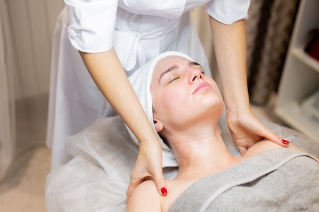 A young beautiful girl lies on the beautician's table and receives procedures, a light facial massage using oil.