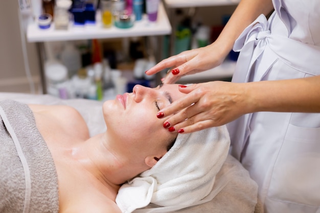 A young beautiful girl lies on the beautician's table and receives procedures, a light facial massage.