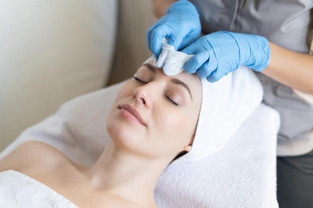 A young beautiful girl lies on the table at the beautician and receives facial cleansing procedures, makeup removal with white wipes