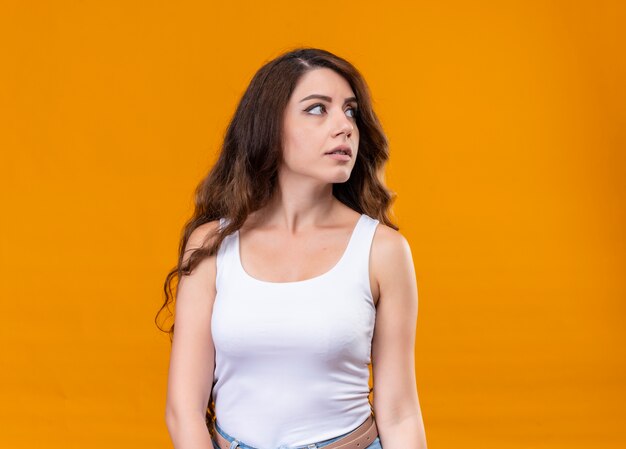 Young beautiful girl looking at right side on isolated orange wall with copy space