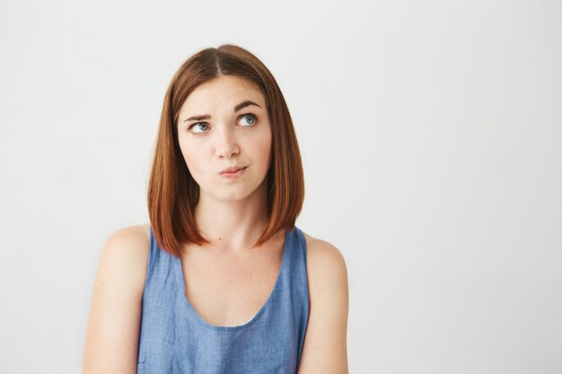 Young beautiful girl looking up thinking raising brow .