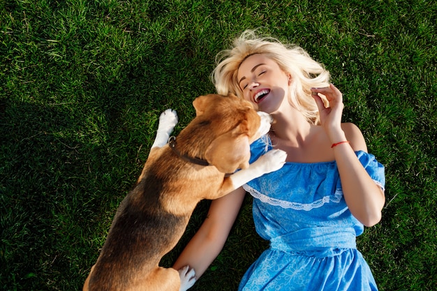 Young beautiful girl lying with beagle dog on grass in park.
