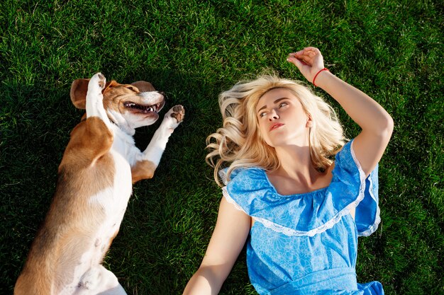 Young beautiful girl lying with beagle dog on grass in park.