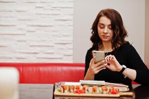 A young beautiful girl making photo by phone of sushi on traditional japanese restaurant