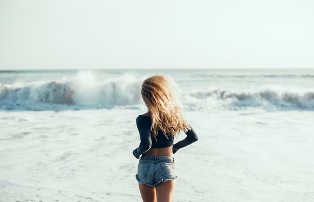 ビーチ、海、波、鮮やかな日差しと日焼けした肌でポーズを取る若い美しい少女