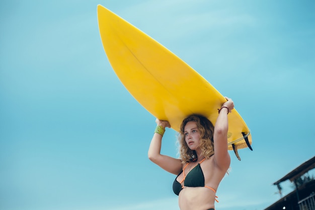 Free photo young beautiful girl posing on the beach with a surfboard, woman surfer, ocean waves