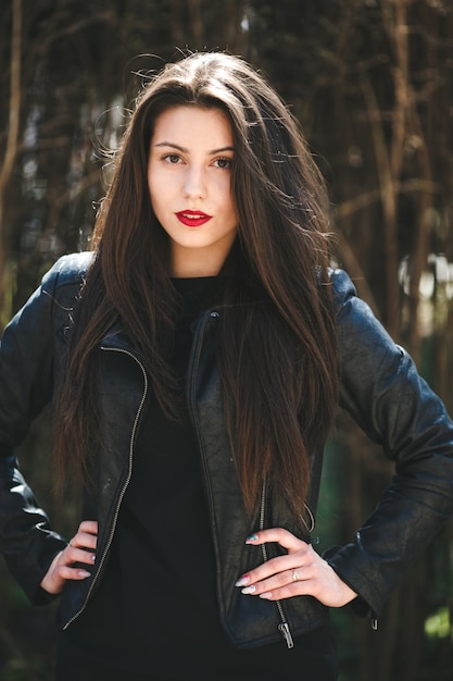 Young beautiful girl posing in a black leather jacket in the park