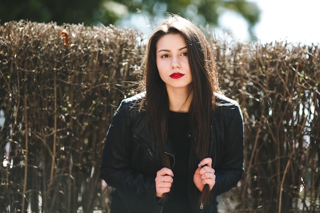 Young beautiful girl posing in a black leather jacket in the park