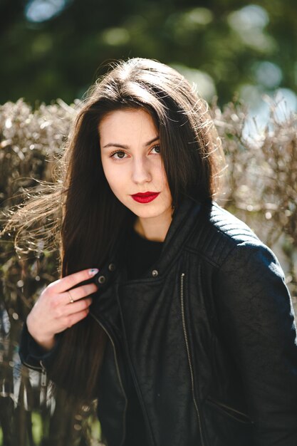 Молодая красивая девушка позирует в черной кожаной куртке в парке