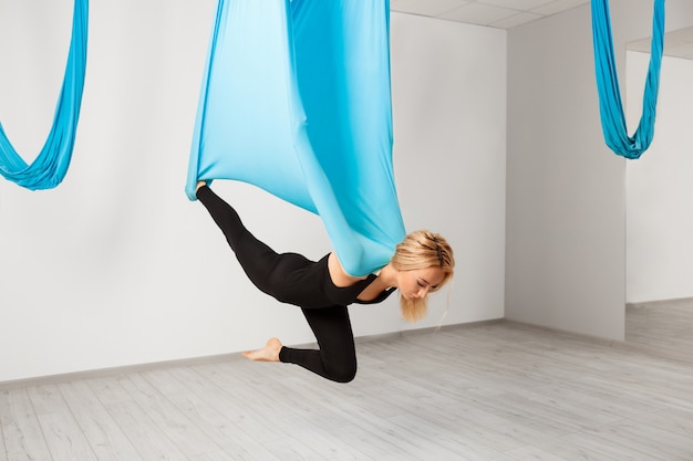 Young beautiful girl practicing aerial yoga in gym.