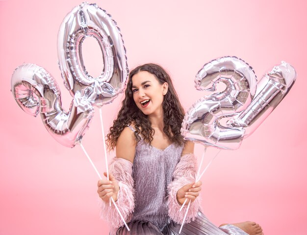 Young beautiful girl rejoices in the new year on a pink background with silver balloons for the new year concept
