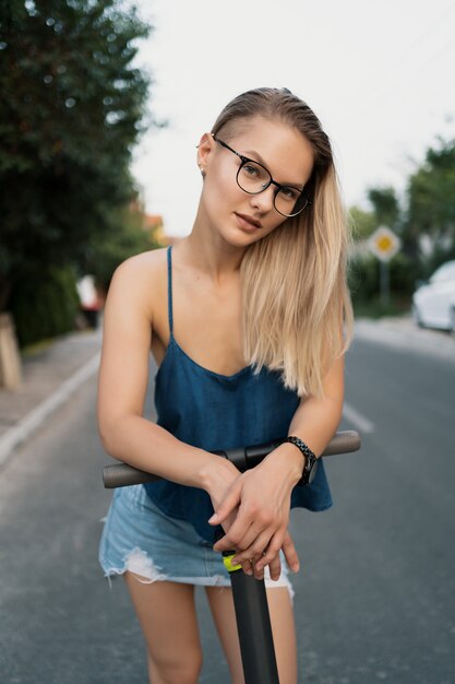 Young beautiful girl riding an electric scooter in the summer on the street