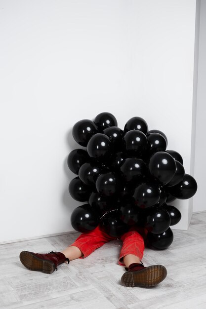 Young beautiful girl sitting in black baloons over white wall