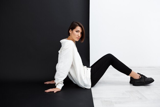 Young beautiful girl sitting on floor over black and white wall