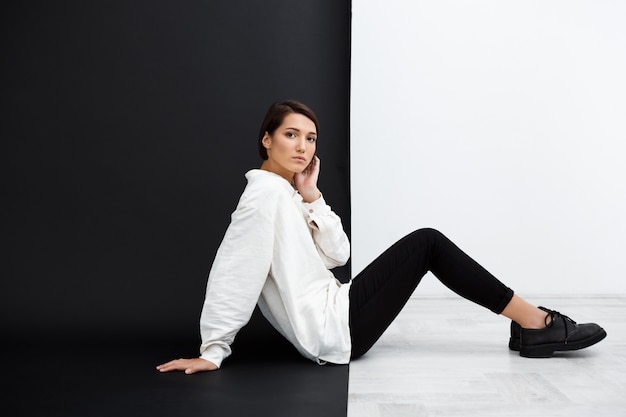 Young beautiful girl sitting on floor over black and white wall