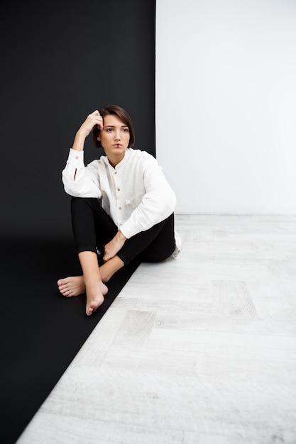 Young beautiful girl sitting on floor over black and white wall