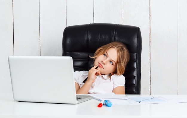 Giovane bella ragazza che si siede al posto di lavoro in ufficio.