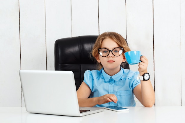 Giovane bella ragazza che si siede al posto di lavoro in ufficio.