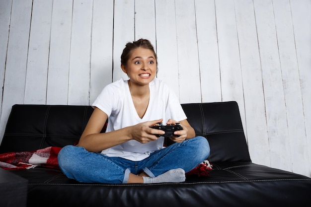 笑顔、ビデオゲーム、自宅のソファに座っている若い美しい少女。スペースをコピーします。