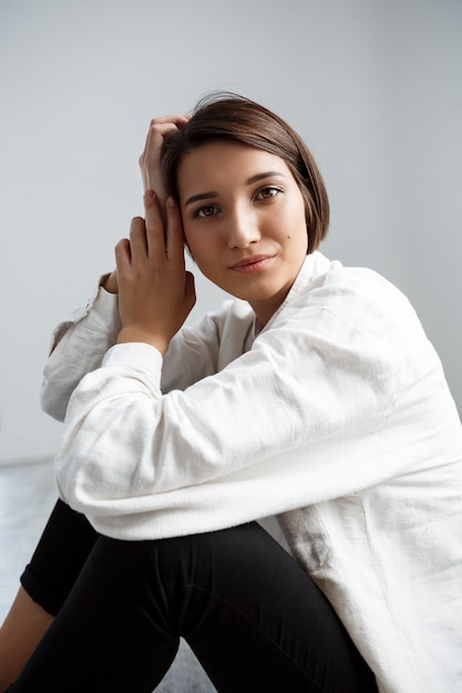 Young beautiful girl smiling sitting on floor over white wall.