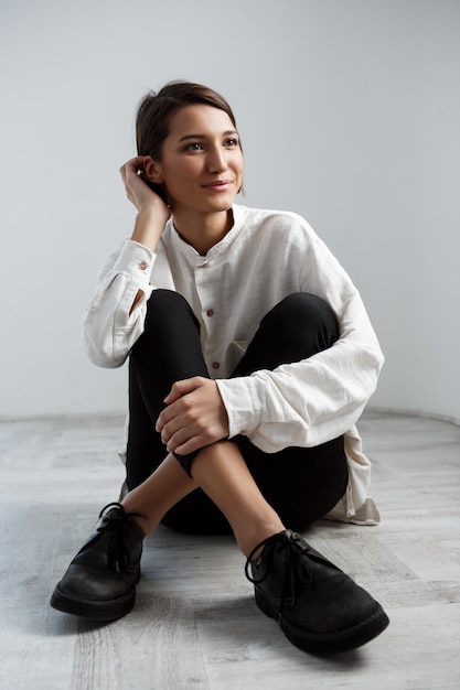 Free photo young beautiful girl smiling sitting on floor over white wall.