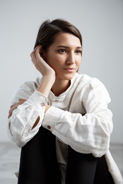 Young beautiful girl smiling sitting on floor over white wall.