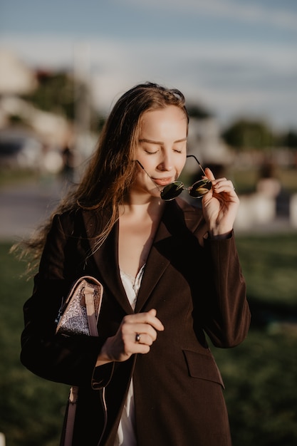 Young beautiful girl in stylish sunglasses and with a fashionable bag at sunset.