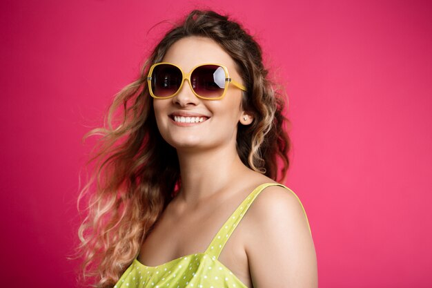 Young beautiful girl in sunglasses smiling over pink wall.