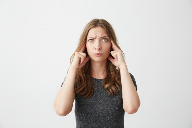 Young beautiful girl thinking with fingers on temples looking up .