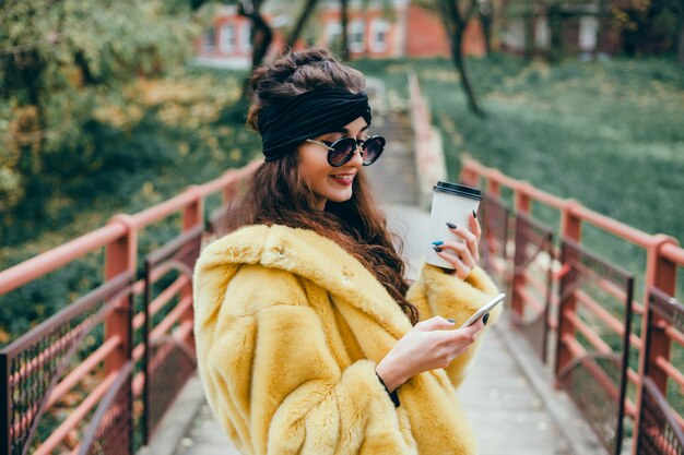 молодая красивая девушка использует смартфон на улице, серфинг в Интернете и пить кофе