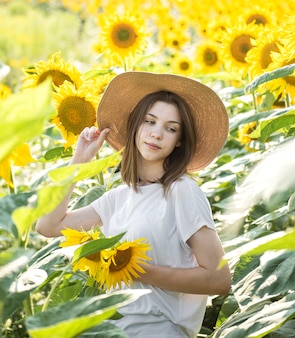 Young beautiful girl walks in the summer in a field with blooming sunflowers