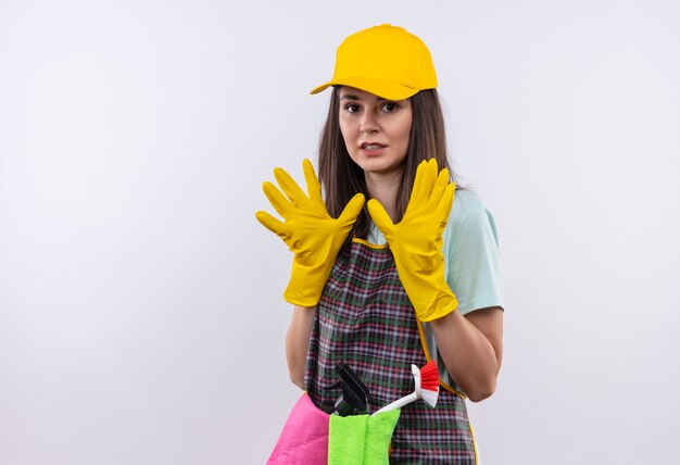 Young beautiful girl wearing apron, cap and rubber gloves making defense gesture with hands scared 