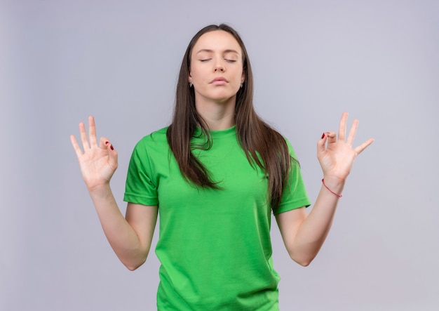 Young beautiful girl wearing green t-shirt relaxing with eyes closing doing meditation gesture with fingers standing over isolated white background