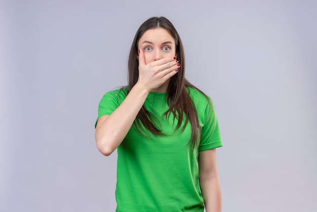 Young beautiful girl wearing green t-shirt shocked covering mouth with hand standing over isolated white background