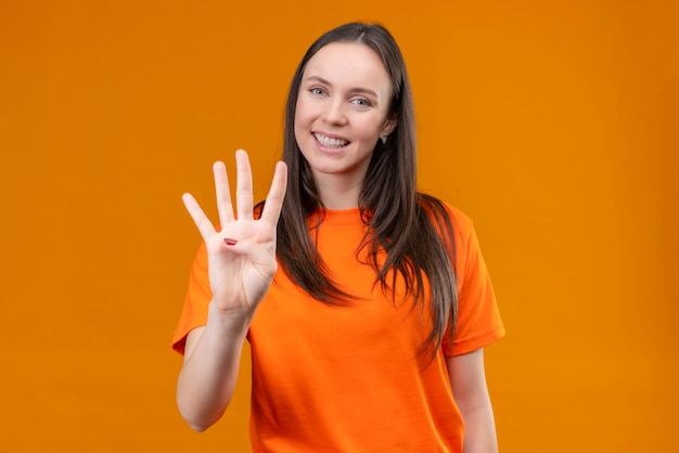 Free photo young beautiful girl wearing orange t-shirt showing and pointing up with fingers number four standing over isolated orange background