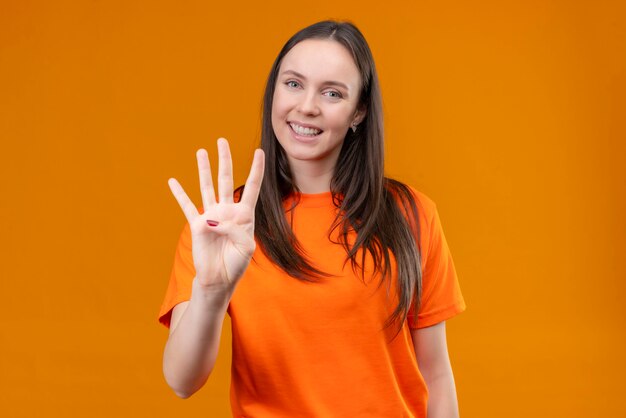 Young beautiful girl wearing orange t-shirt showing and pointing up with fingers number four standing over isolated orange background