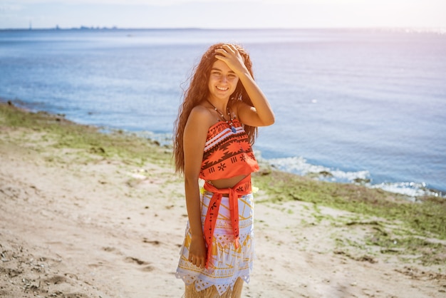 A young beautiful girl with long hair walks on the beach, posing against the sea on a sunny summer day