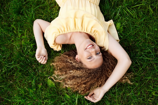 Young beautiful girl in yellow dress lying on grass.