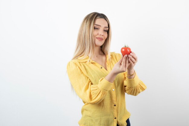 Young beautiful girl in yellow shirt looking at red tomato on white.