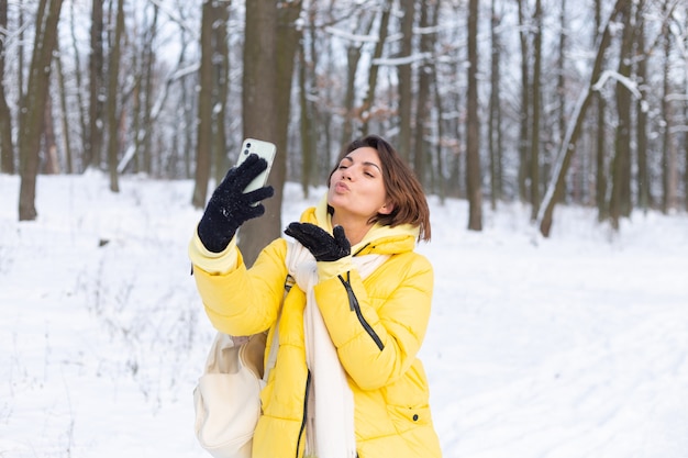 Young beautiful happy cheerful woman in the winter forest video blog, makes a selfie photo