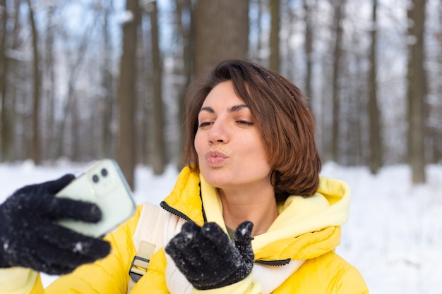 Young beautiful happy cheerful woman in the winter forest video blog, makes a selfie photo