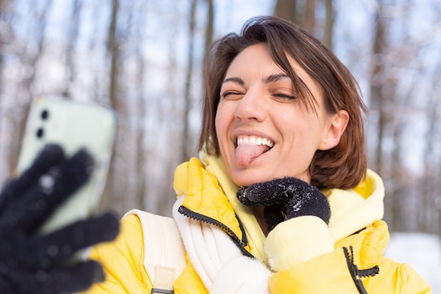 Young beautiful happy cheerful woman in the winter forest video blog, makes a selfie photo