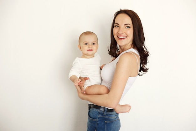 Free photo young beautiful happy mother smiling laughing holding her baby daughter over white wall.