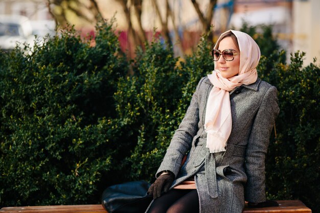 Young beautiful happy woman in a coat sitting on a bench in the park