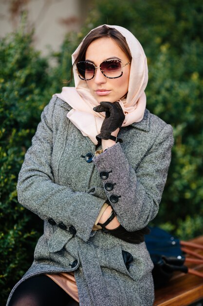 Young beautiful happy woman in a coat sitting on a bench in the park