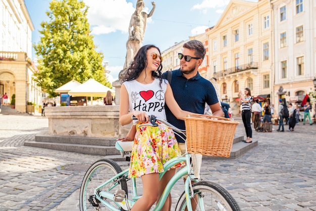 Young beautiful hipster couple in love walking with bicycle on old city street