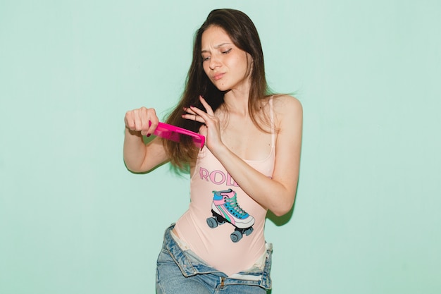 Young beautiful hipster woman posing against blue wall, combing long hair