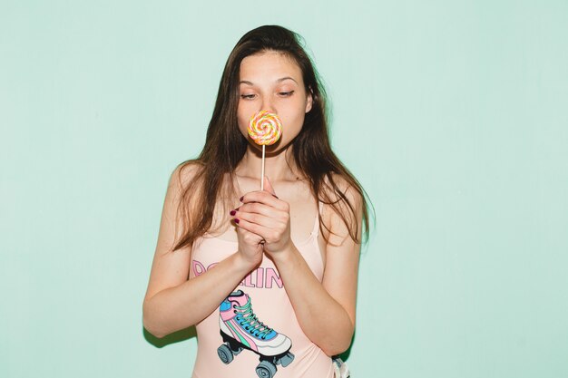 Young beautiful hipster woman posing against blue wall, holding lolly pop candy