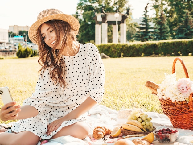 트렌디한 여름 청바지, 분홍색 티셔츠, 모자를 쓴 젊고 아름다운 힙스터 여성. 바깥에서 피크닉을 하는 평온한 여자.