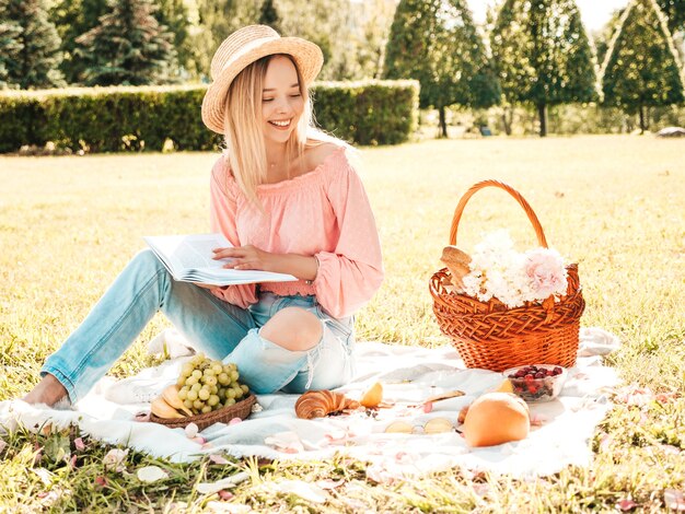 Young beautiful hipster woman in trendy summer jeans, pink T-shirt and hat. Carefree woman making picnic outside. 